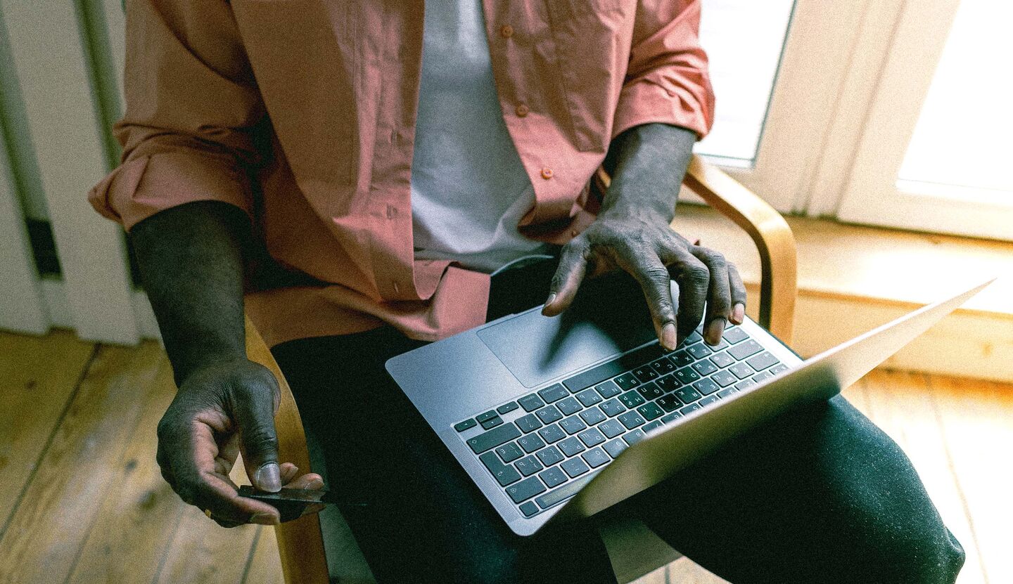 Hände eines Mannes, die eine Keditkarte halten, während er auf seinem Laptop arbeitet.