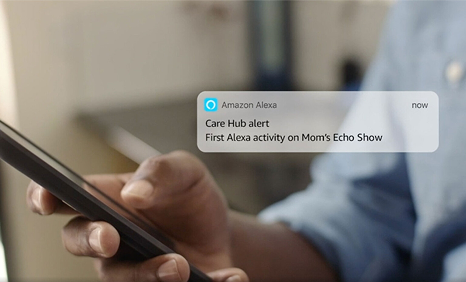 Closeup of a person holding their mobile phone. A message from Amazon Alexa being shown next to it says: "Care Hub alert - First Alexa activity on Mom's Echo Show"